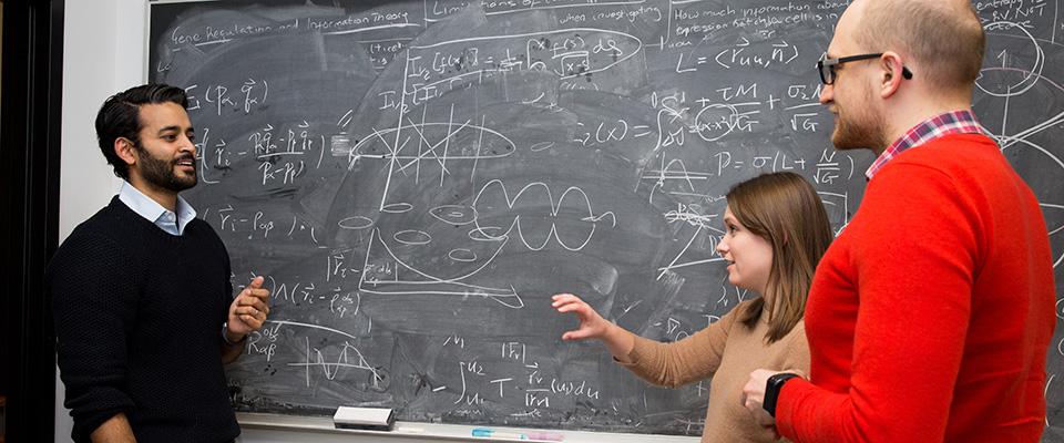 Three people standing at chalkboard with equations