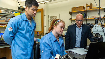 Two people in labcoats and professor at laptop