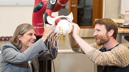 Two smiling people touching a robot cat