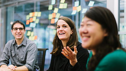 Three people in discussion in front of glass wall with post-its